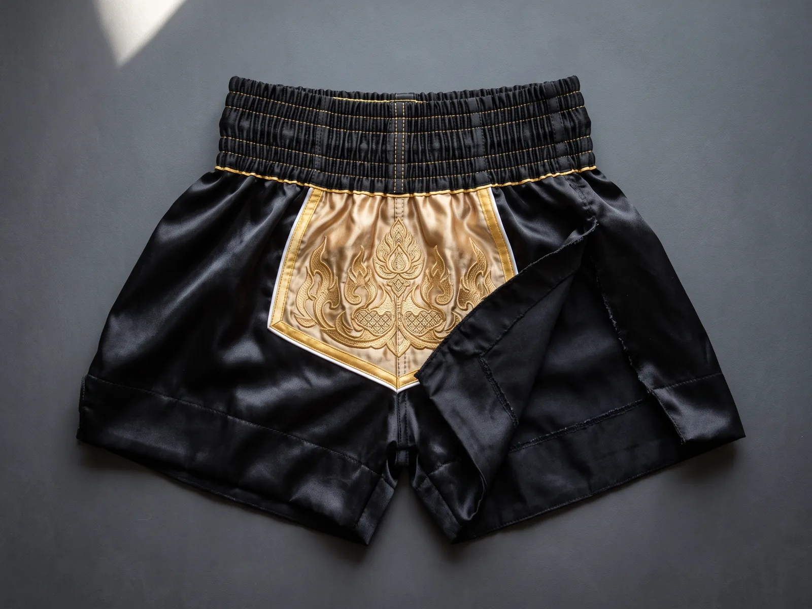 Custom Muay Thai shorts manufacturer flat-lay of satin fight shorts with contrast waistband