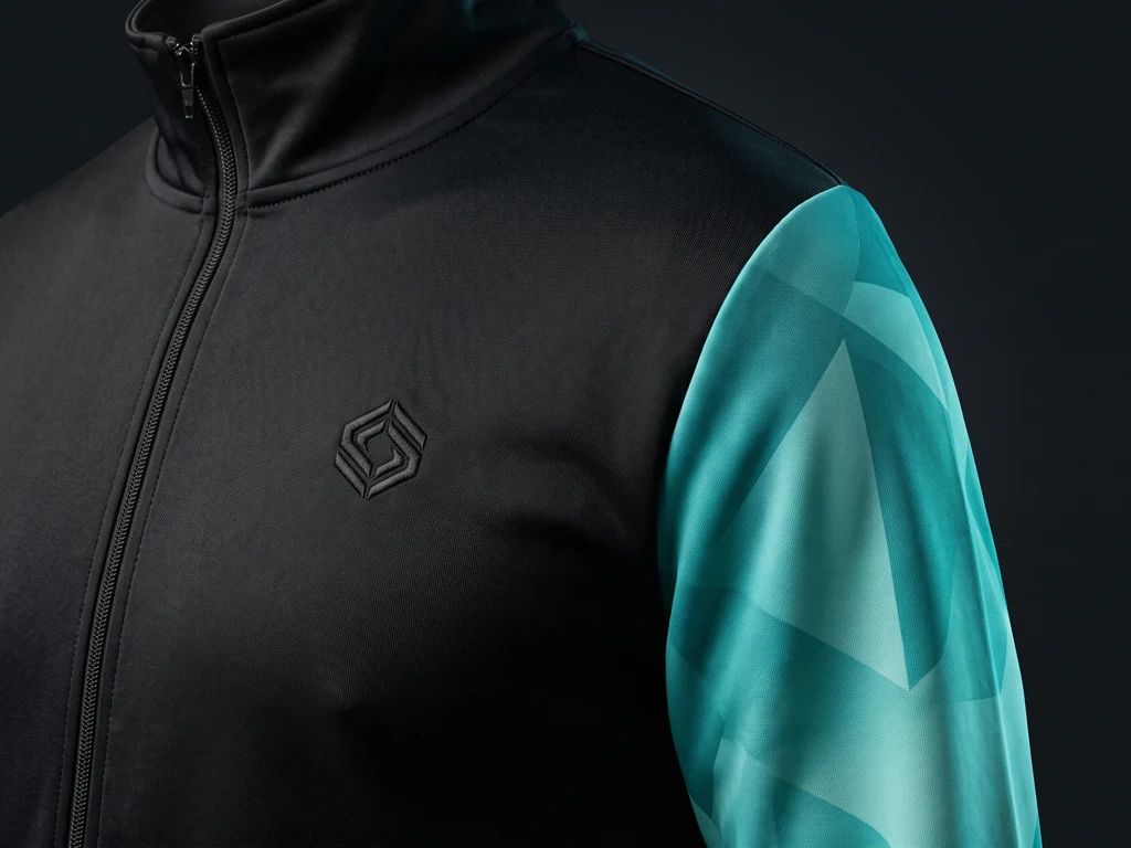 Tracksuit jacket decoration detail: tonal embroidered chest mark and sublimated teal sleeve panel